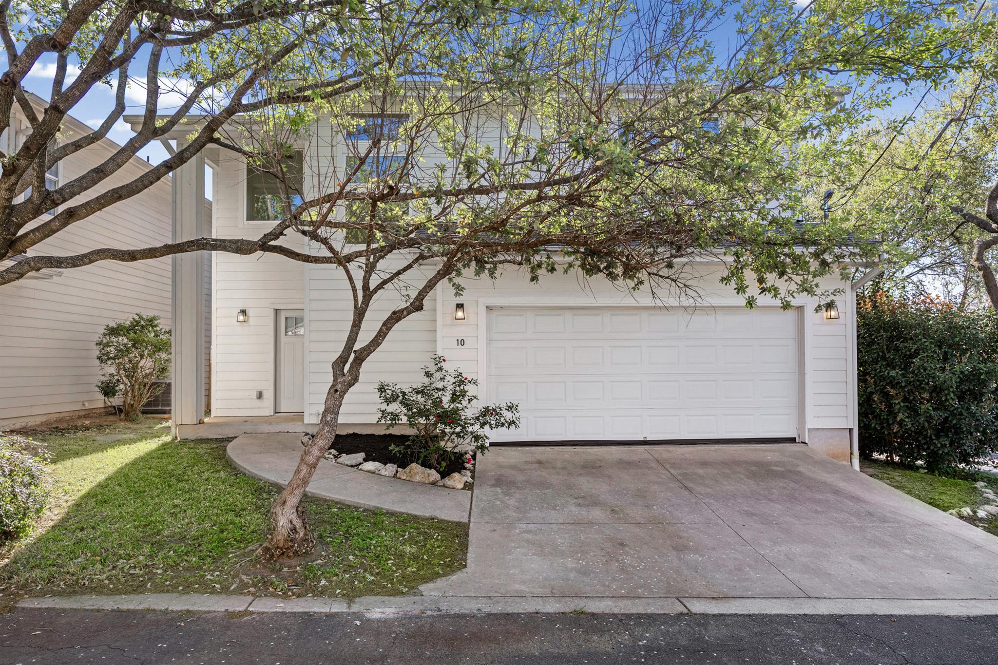 White two-story home with a double garage and a mature tree shading the front.