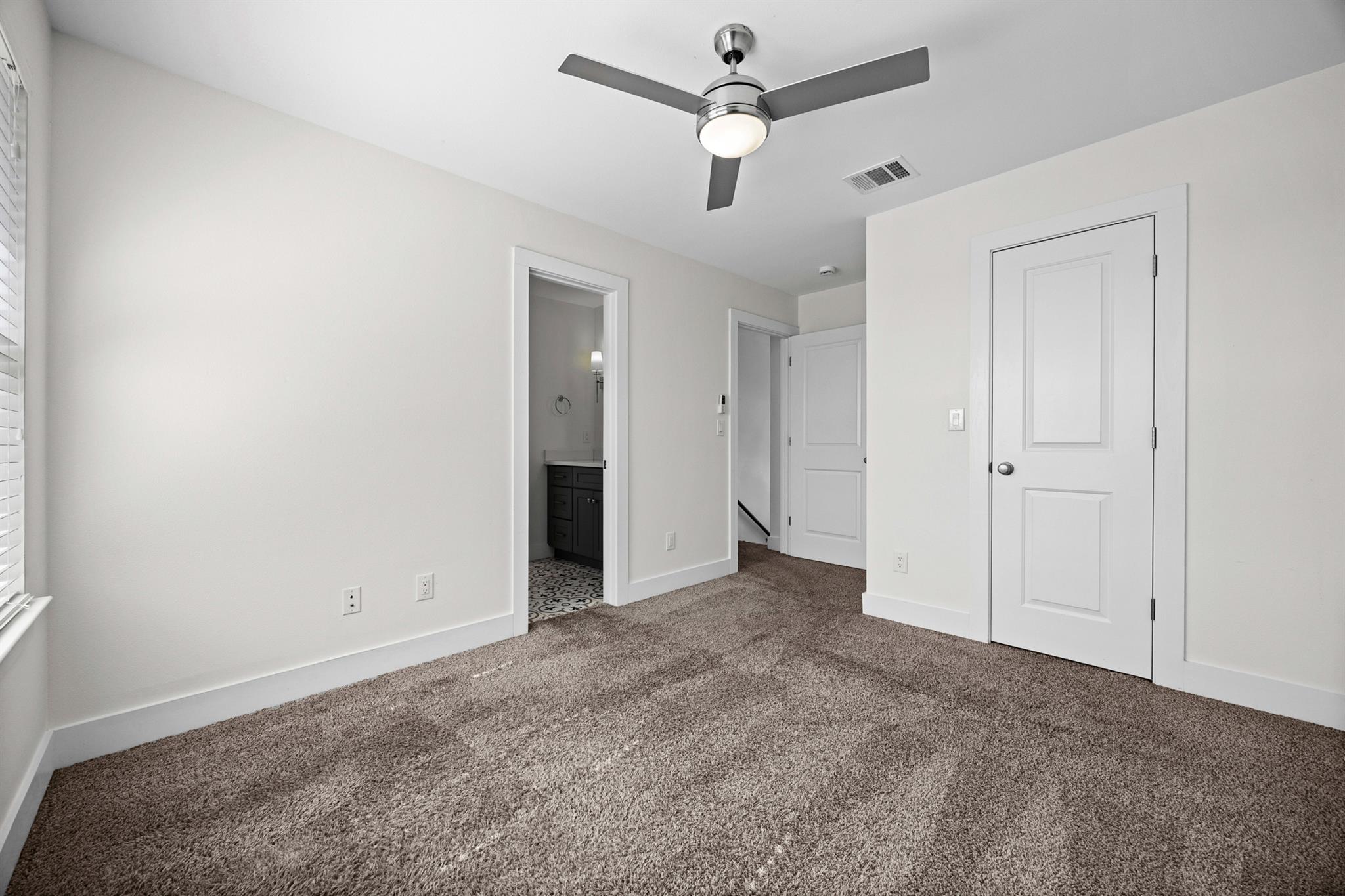 Vacant carpeted bedroom with a ceiling fan and an open doorway to a bathroom.