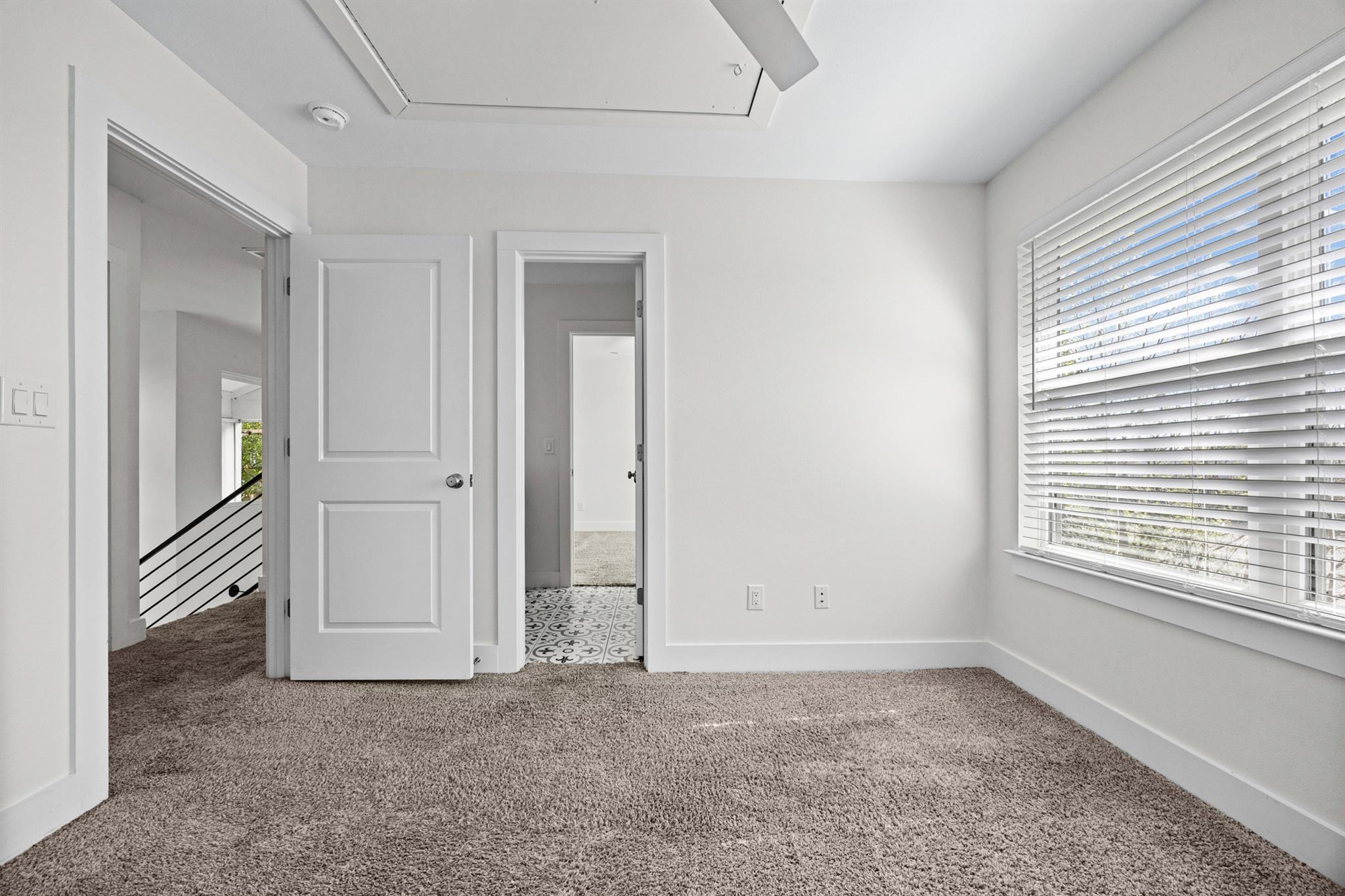 Empty carpeted bedroom with a large window and open doorways.