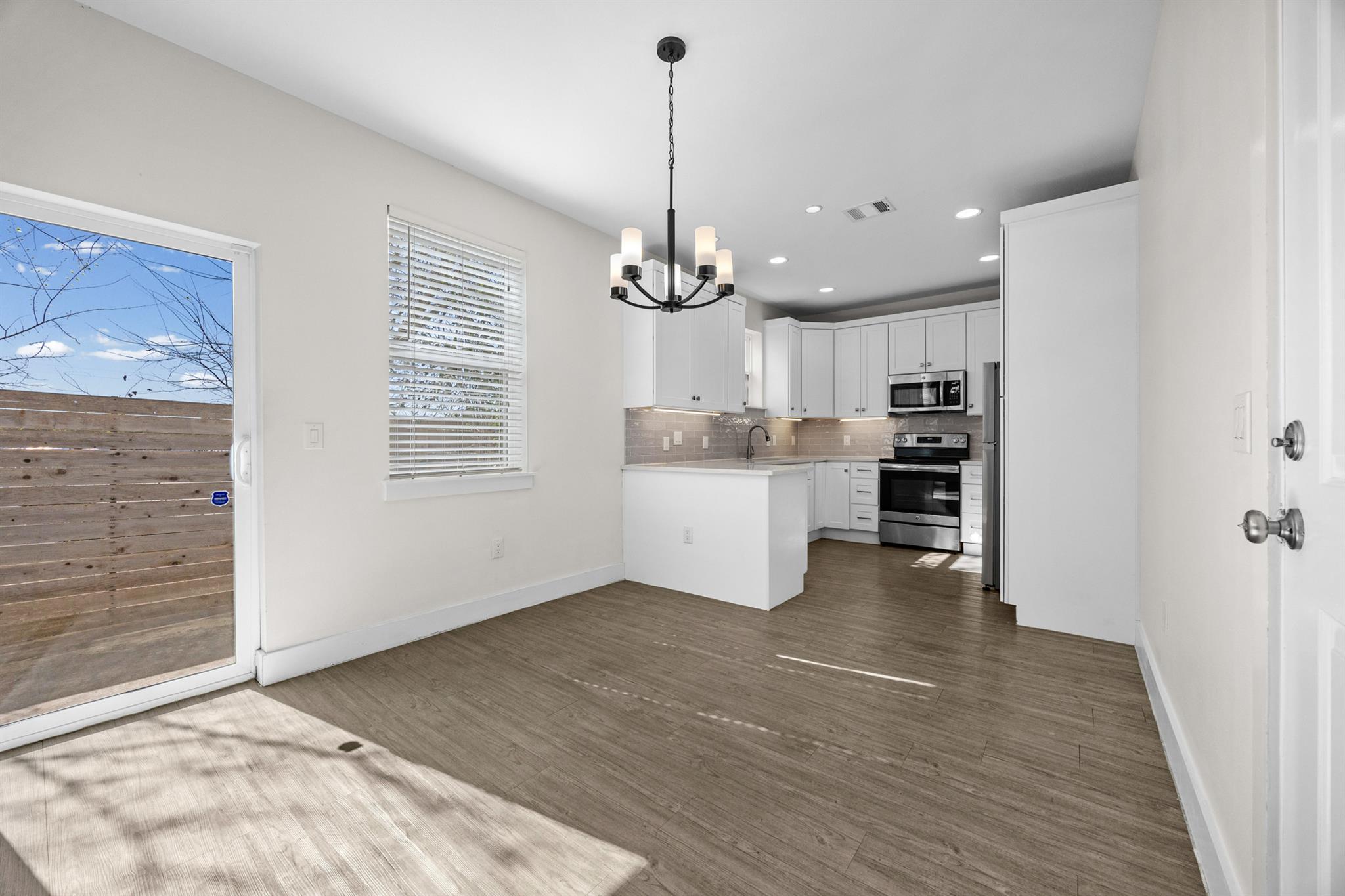 Vacant kitchen with white cabinets, stainless steel appliances, and a peninsula beside a sliding glass door.