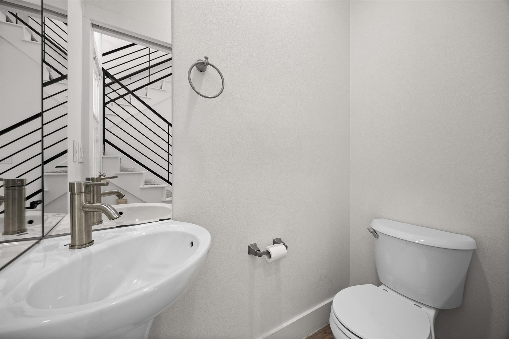 Bathroom with a white sink and toilet; mirror reflects a staircase with black railings.