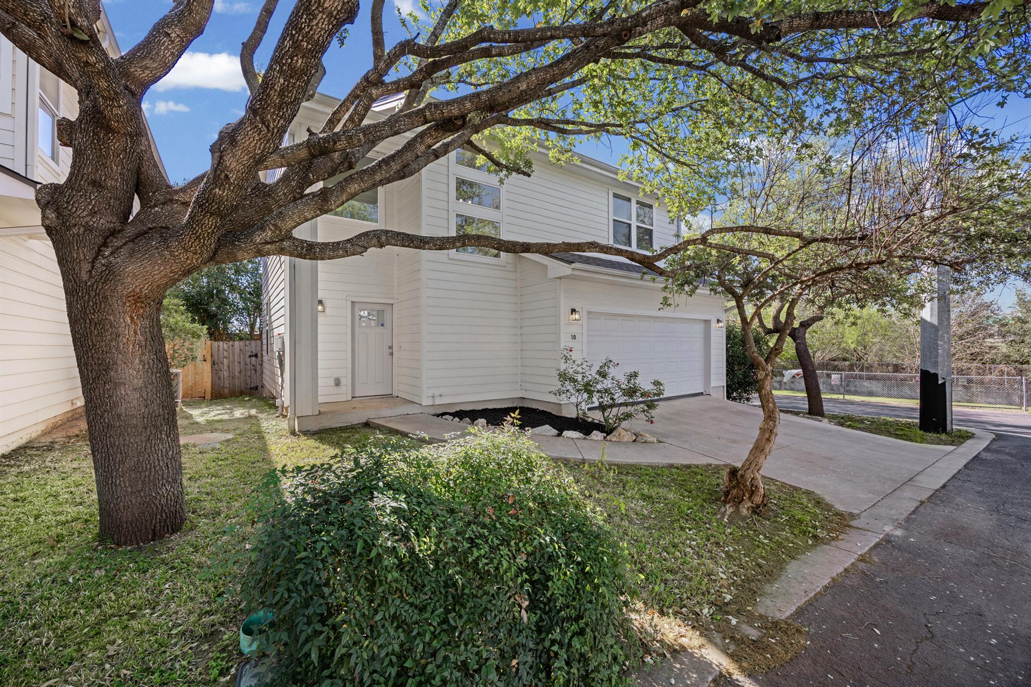 White two-story home with an attached garage, concrete driveway, and large shade trees.