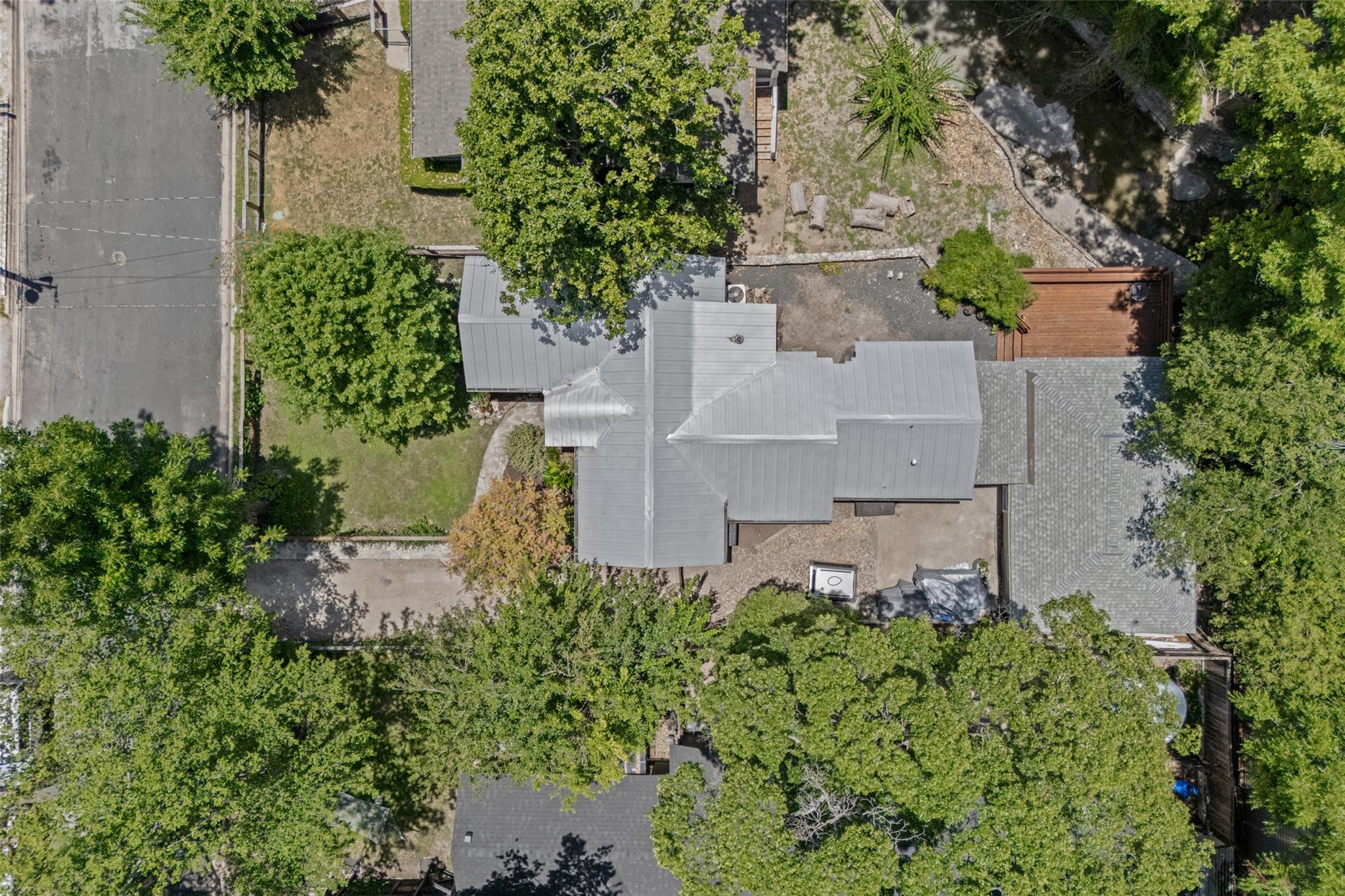 Aerial view of a tree-shaded home with a metal roof and a wooden backyard deck.