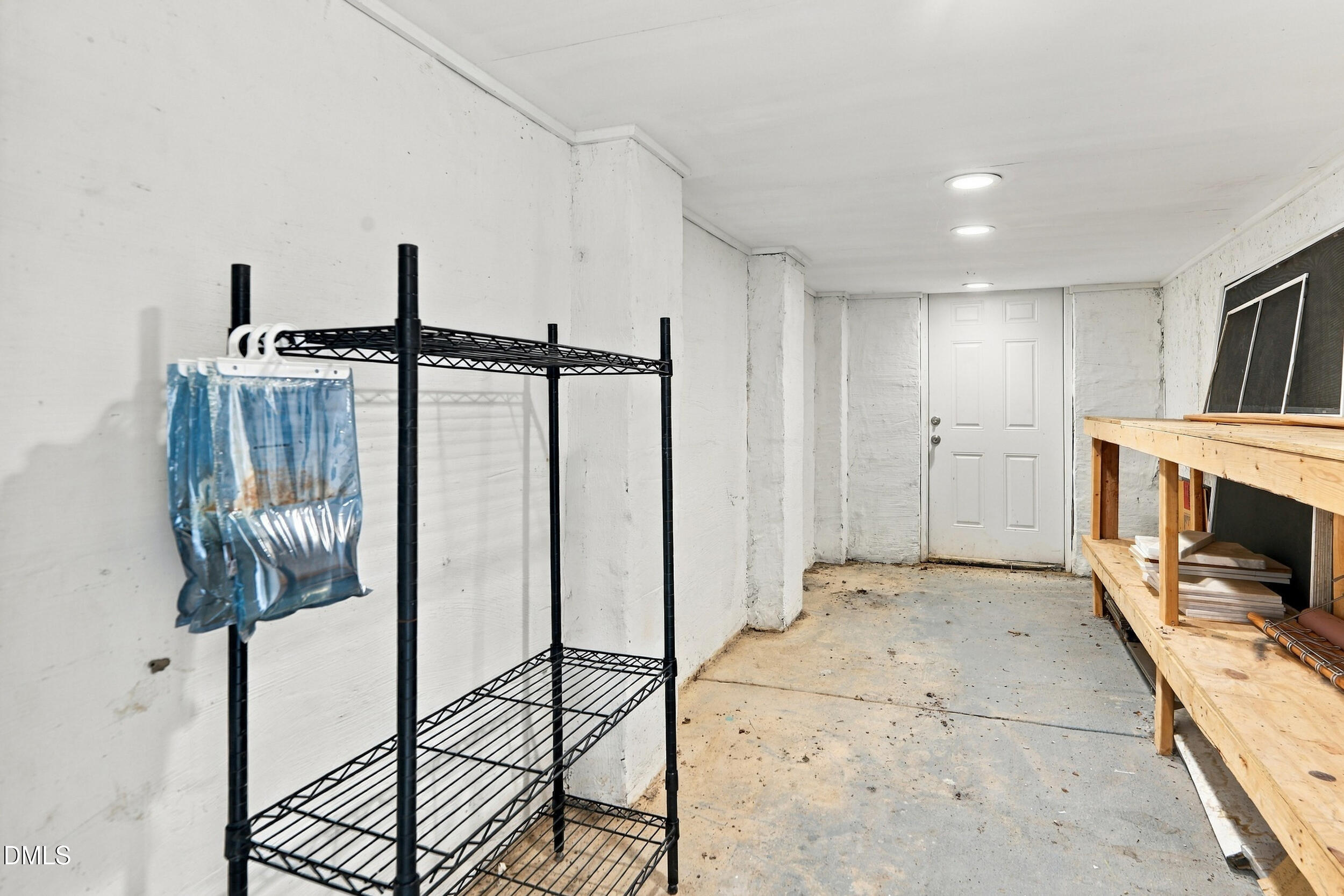 Unfinished basement storage area with metal shelving, a wooden workbench, and a white door.
