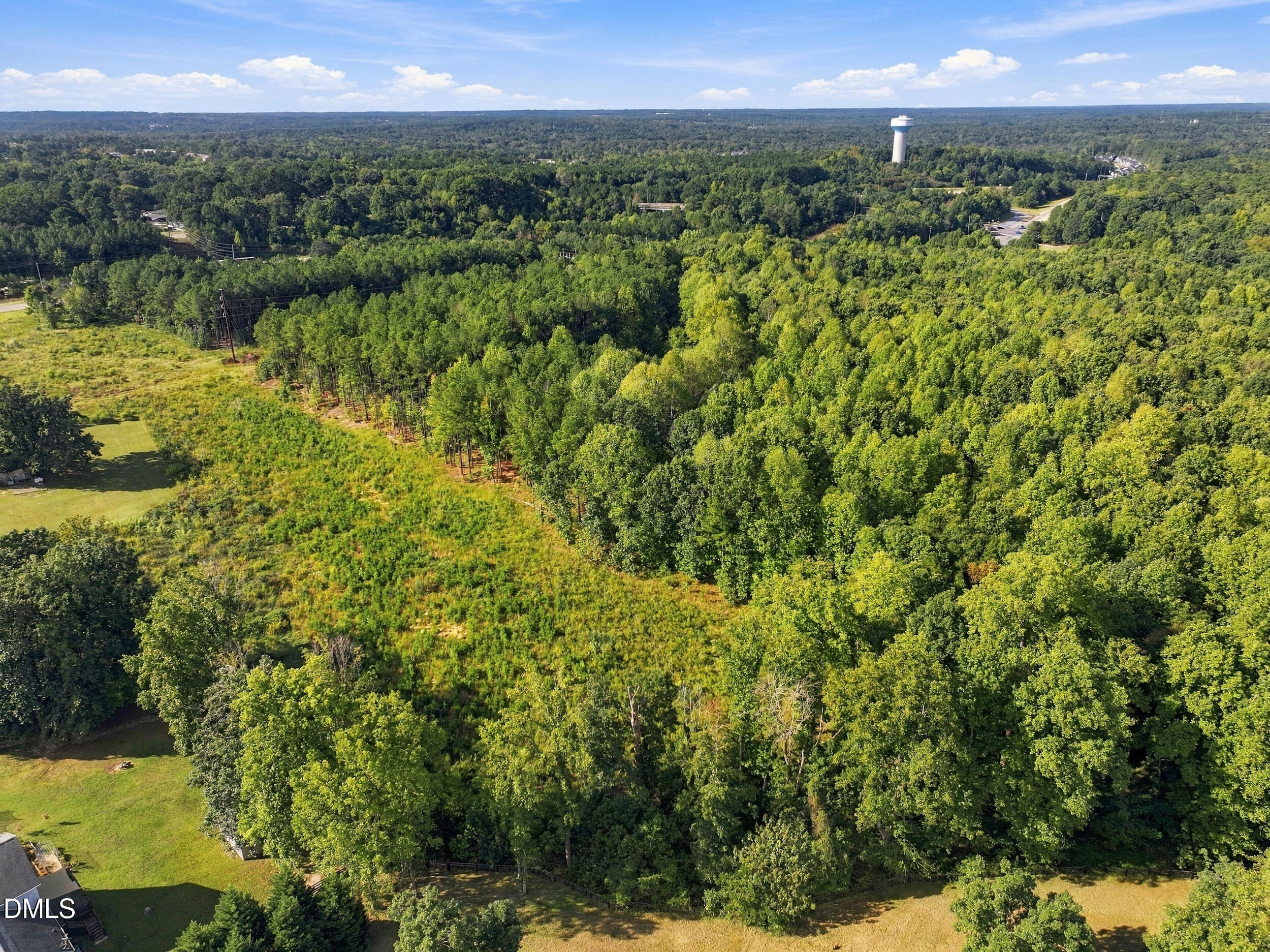 Aerial view of wooded land with a grassy clearing and distant water tower.