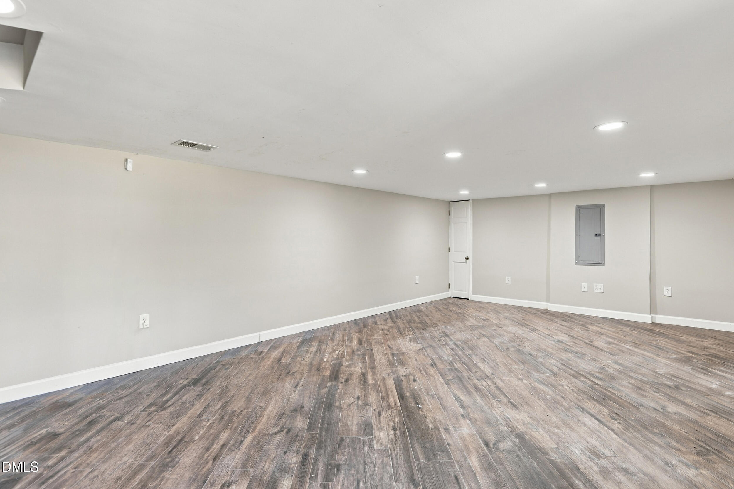 Empty room with gray-brown plank flooring, recessed lights, and an electrical panel.