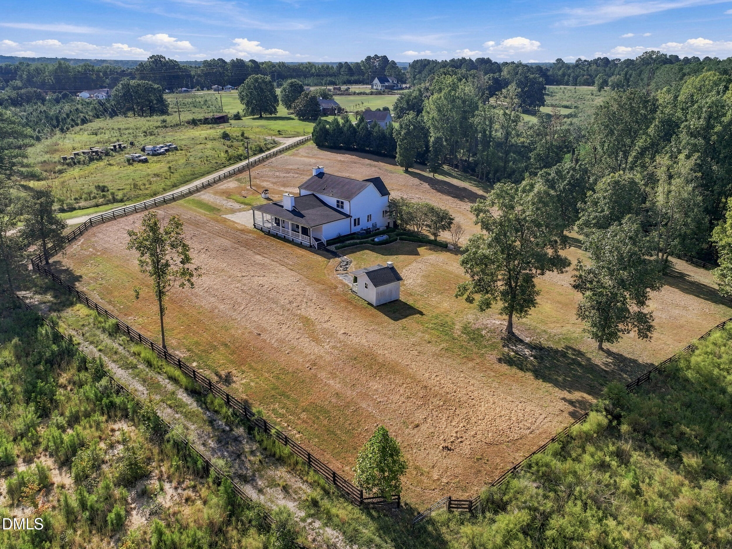 Aerial view of a white two-story house and shed in a large fenced, tree-lined yard.