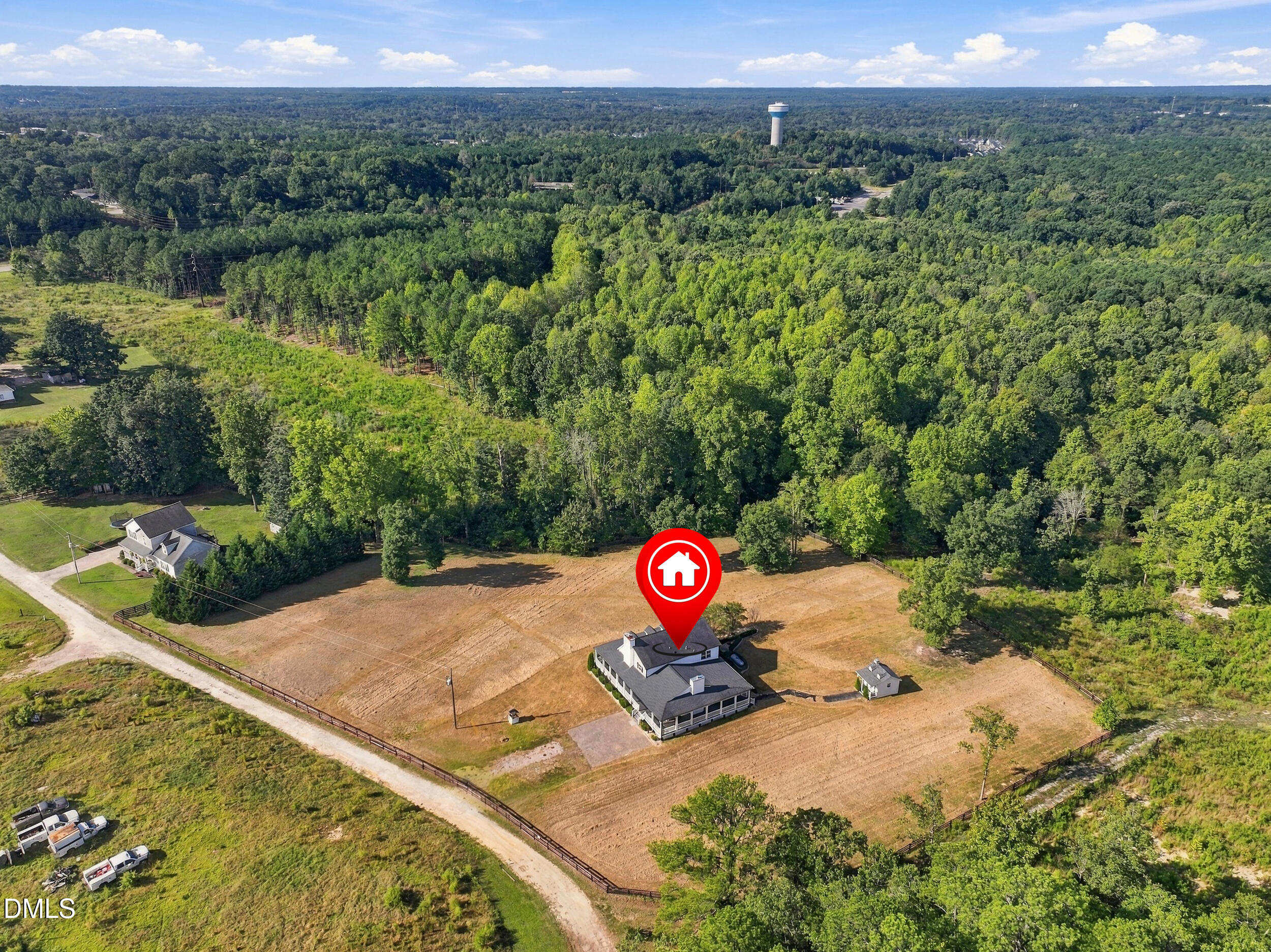 Aerial view of a house on a cleared, fenced lot beside dense woodland.