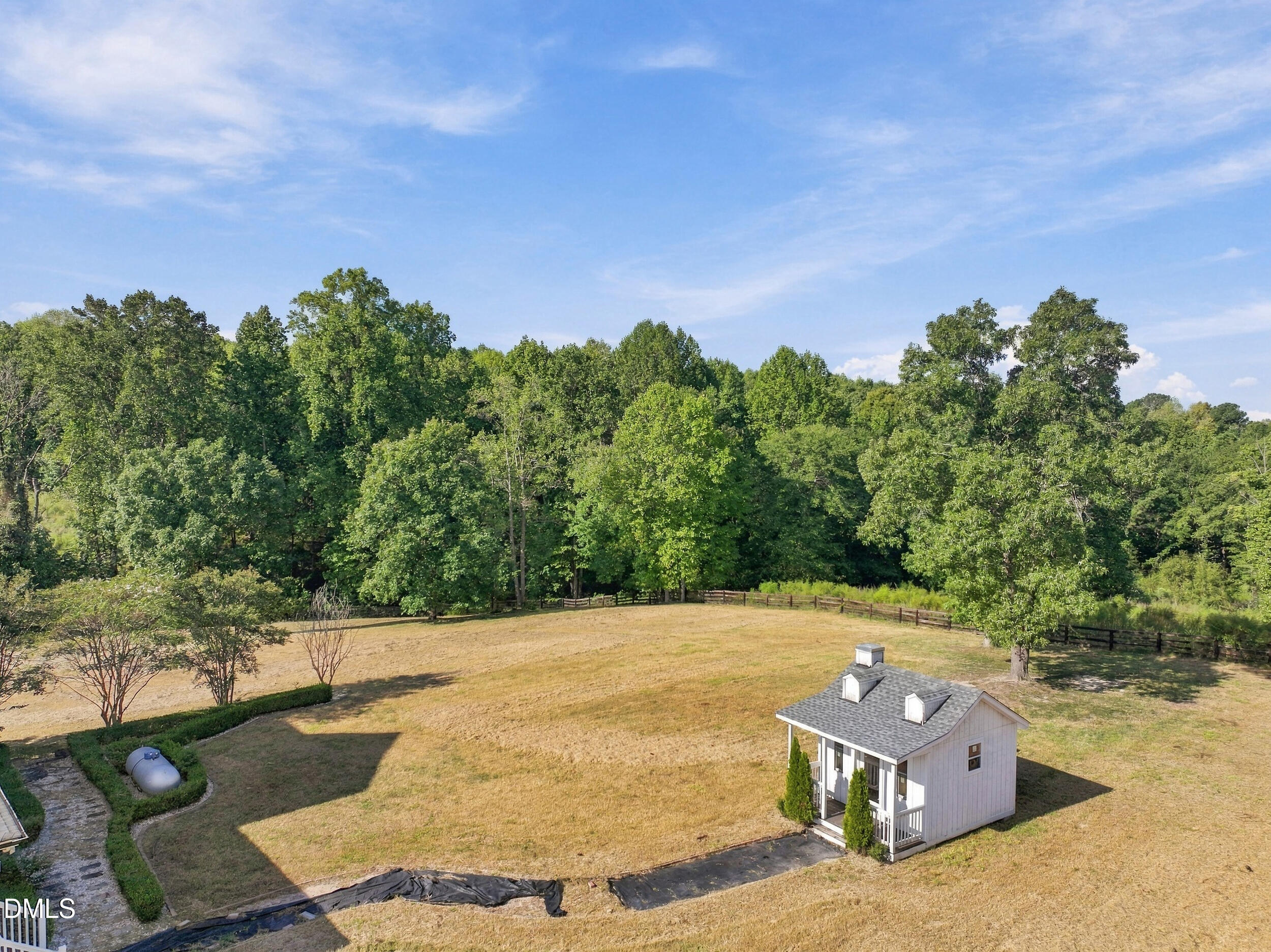 Elevated view of a broad lawn bordered by trees and fencing, with a small white outbuilding.