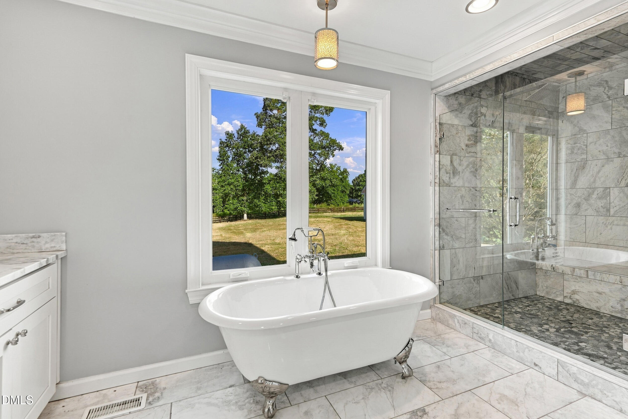 Bathroom with a clawfoot tub beneath a large yard-facing window and a marble-tiled glass shower.