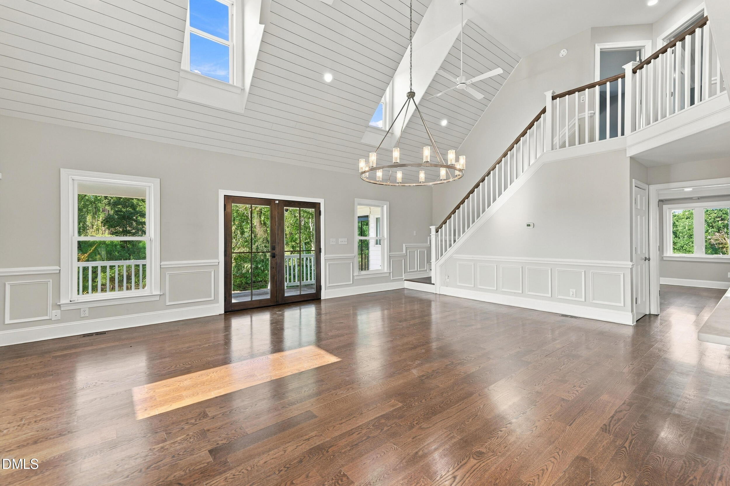 Vacant living room with vaulted ceiling, hardwood floors, and a staircase overlooking the open space.