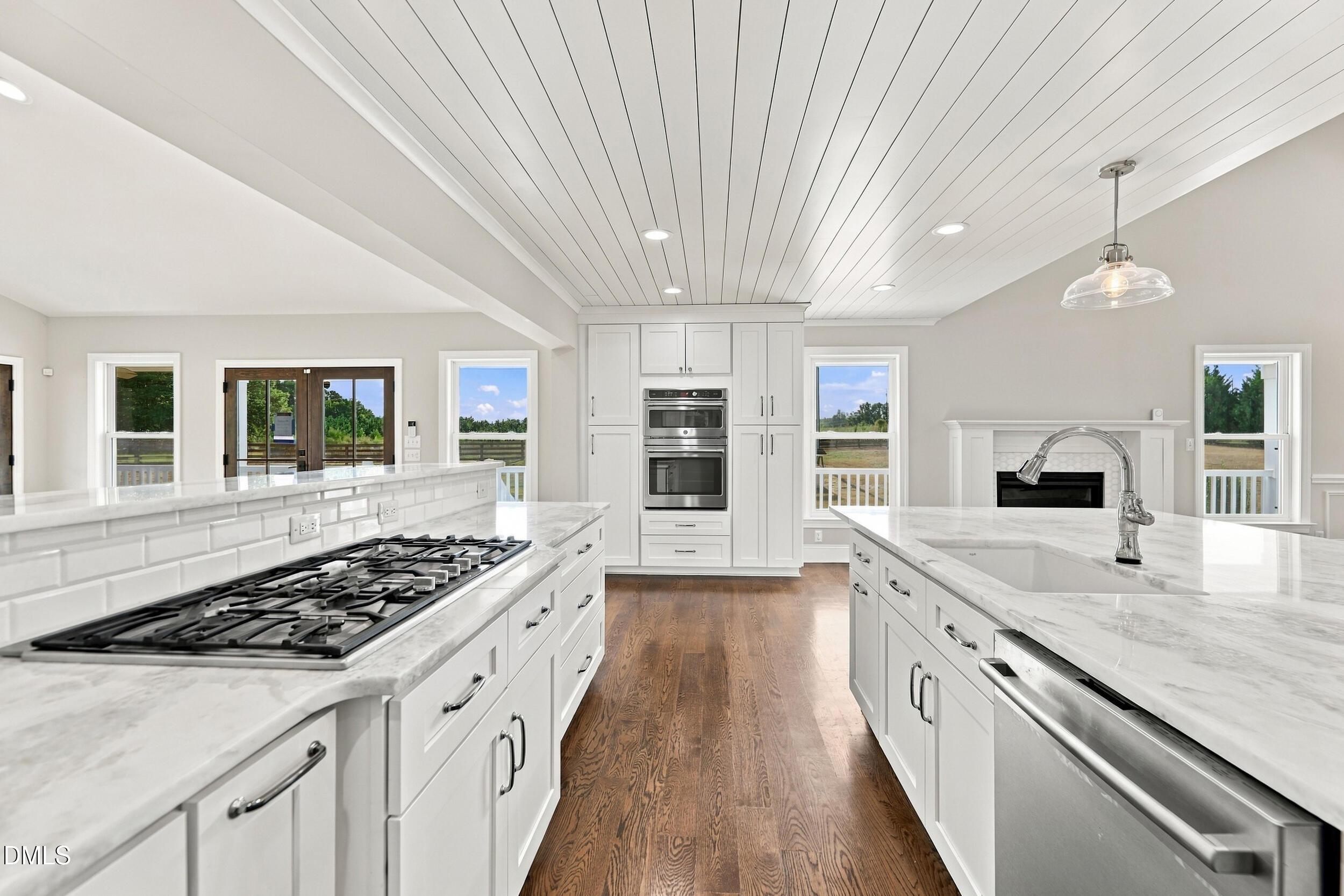 Bright white kitchen with marble counters, two islands, gas cooktop, double ovens, and hardwood floors.