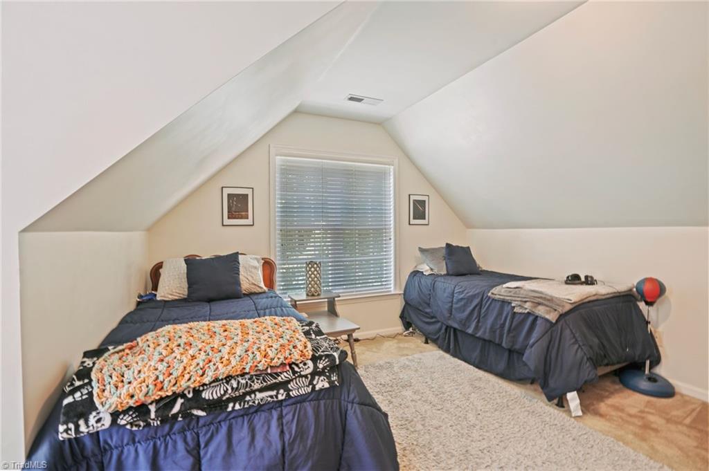 Attic bedroom with two twin beds beneath a sloped ceiling and a central window.