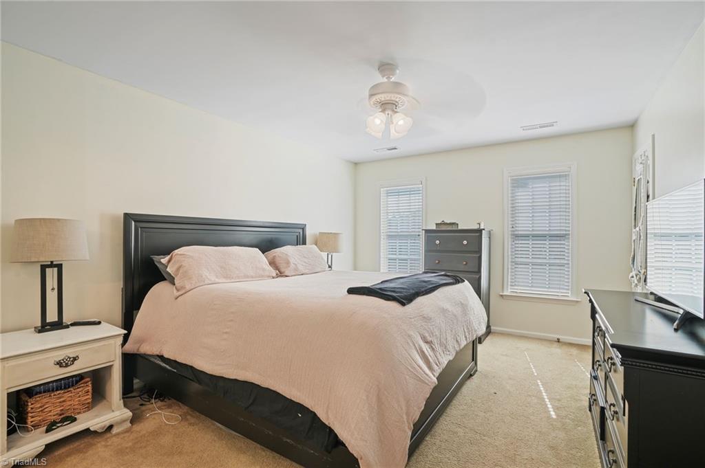 Furnished bedroom with a black bed, pale pink bedding, dark dressers, and windows with blinds.
