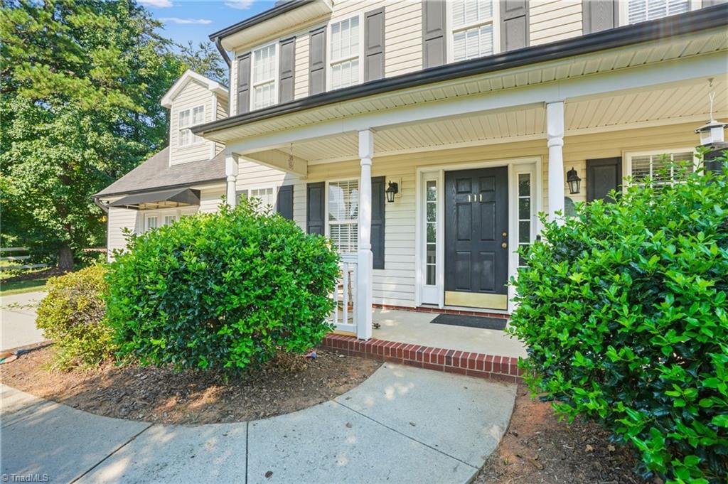 Two-story house with a covered porch, black front door, and shrubs along the walkway.