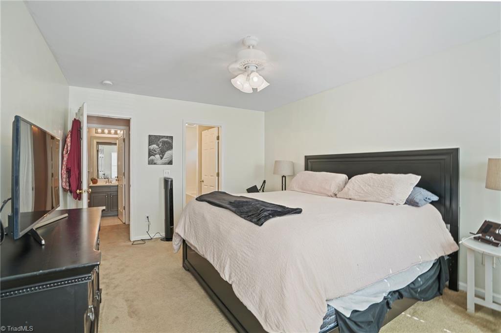 Furnished bedroom with a large bed, dark headboard, and doorway to an ensuite bathroom.