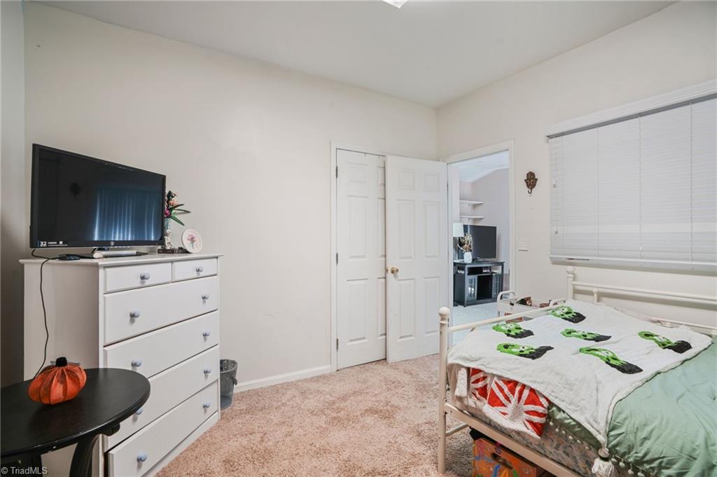 Bedroom with a white metal bed, patterned bedding, and a dresser topped by a television.