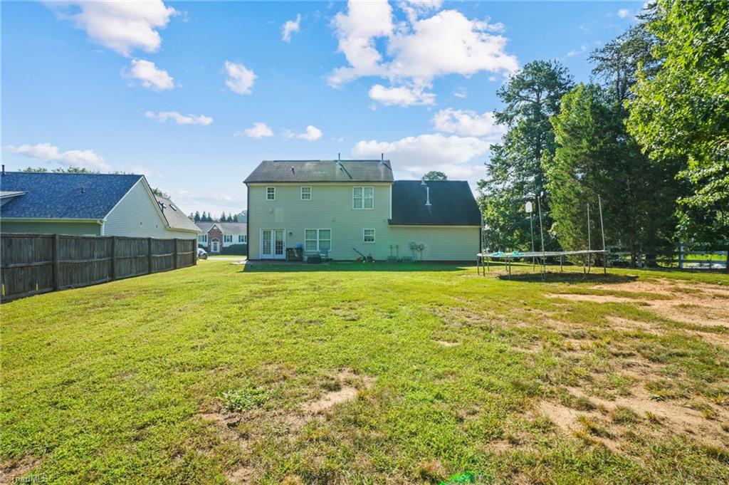 Rear of a light-green two-story house beyond a broad lawn, with a trampoline and privacy fence.