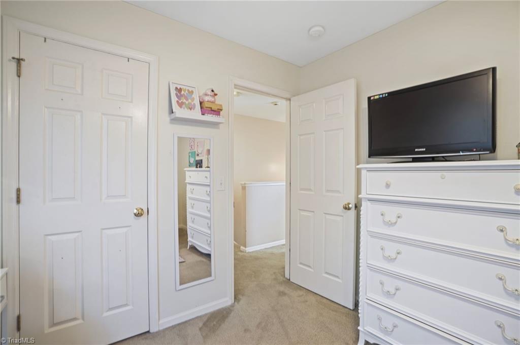 Bedroom with beige carpet, white dressers, wall mirror, and television.