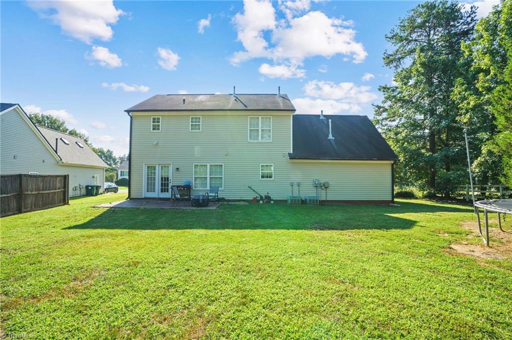 Rear of a light-green two-story house with patio furniture and a broad lawn.