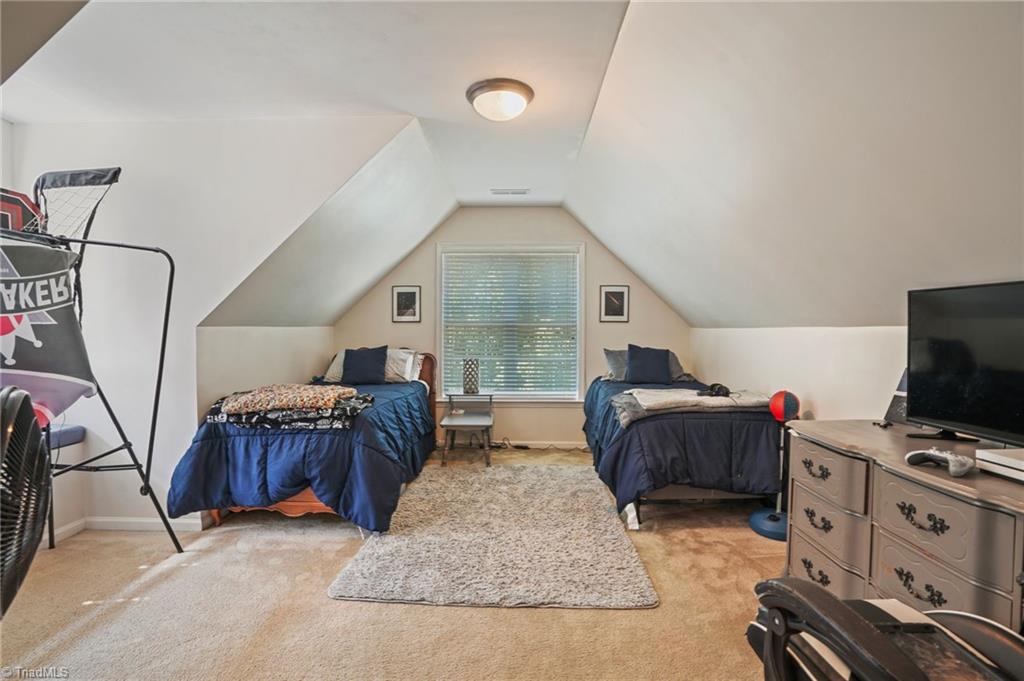 Upstairs bedroom with two navy-covered beds beneath a sloped ceiling and a television on a dresser.