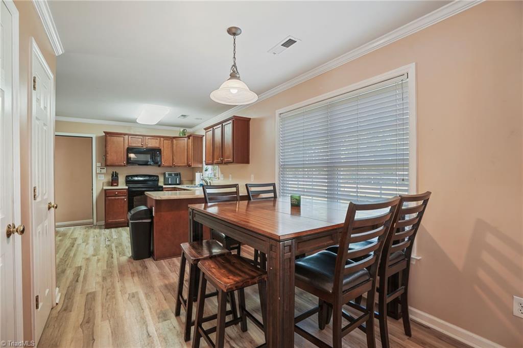 Dining area with a dark wood table and chairs beside a kitchen with wood cabinets and black appliances.