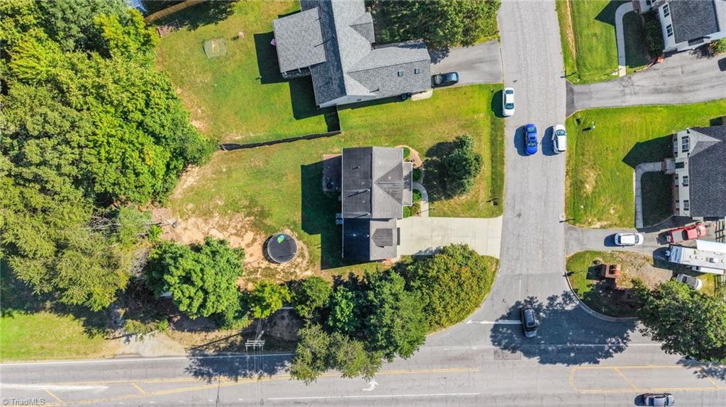 Aerial view of a house and lot with mature trees beside a residential street.