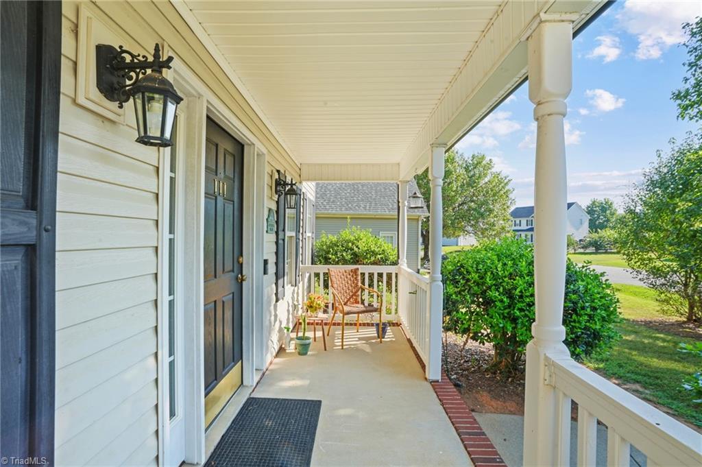 Covered front porch with white columns, a black door, and two chairs overlooking the yard.