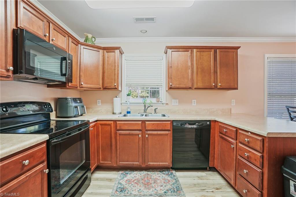 Kitchen with reddish wood cabinets, black appliances, and a sink beneath the window.