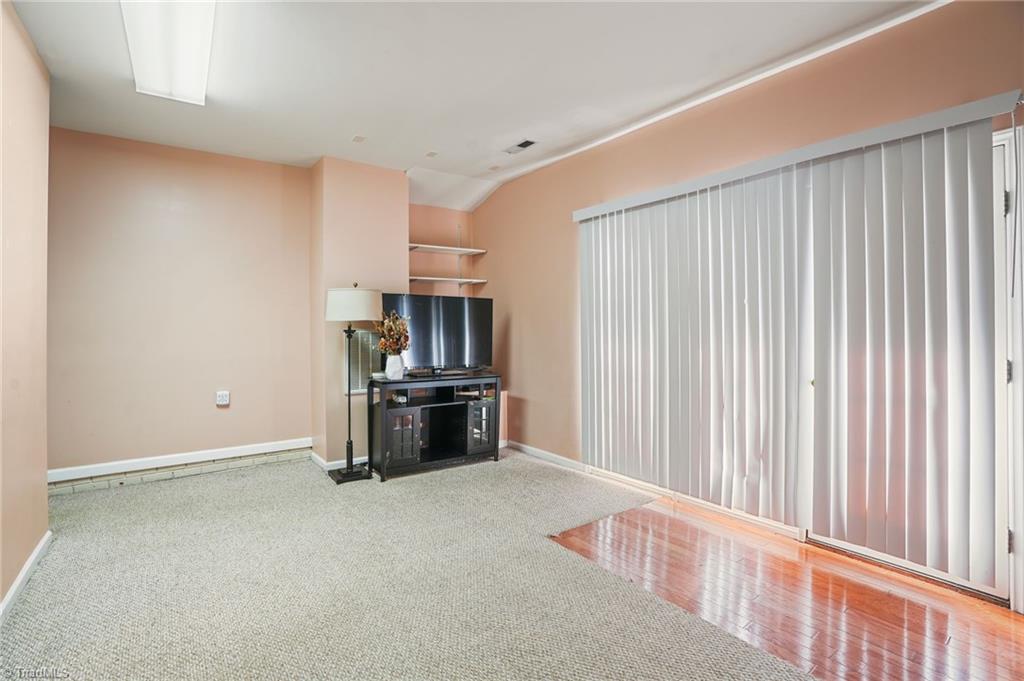 Living room with a TV console, peach walls, carpet, hardwood flooring, and vertical blinds.