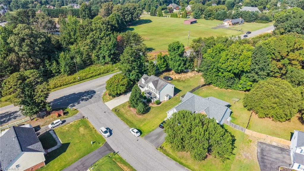 Aerial view of a white two-story house with a lawn and driveway beside a tree-lined street.