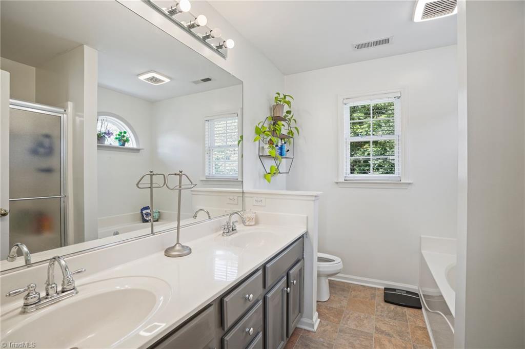 Bathroom with a double-sink vanity, gray cabinets, large mirror, and windows.