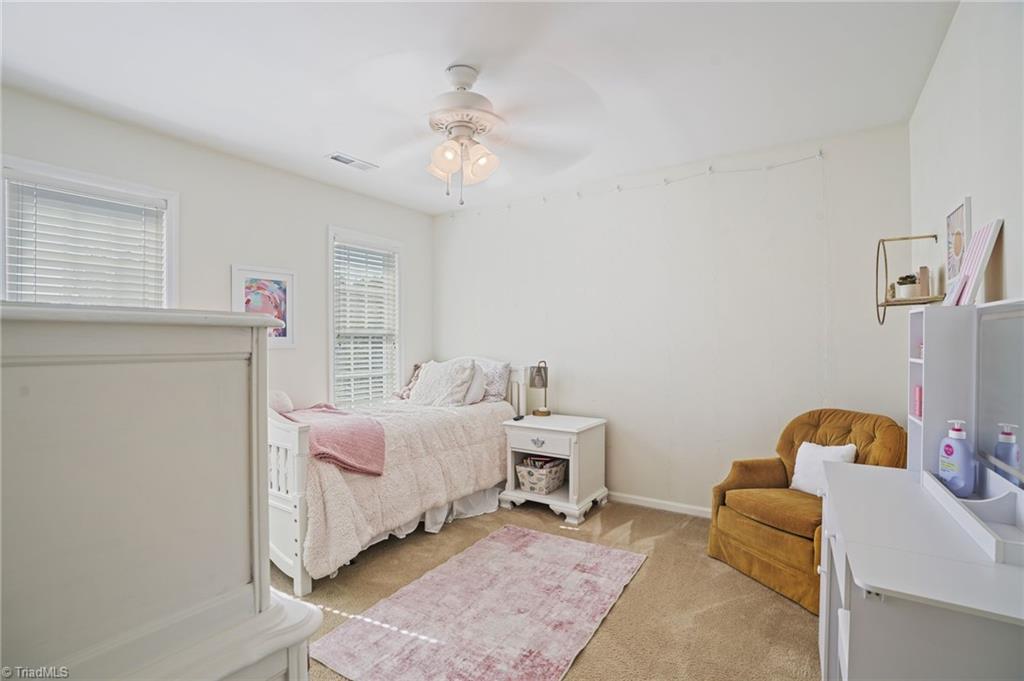Bedroom with a pink-dressed white daybed, mustard-yellow armchair, and pink rug.