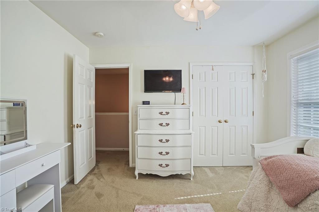 Bedroom with beige carpet, white dresser and vanity, and a pink quilted bedspread.