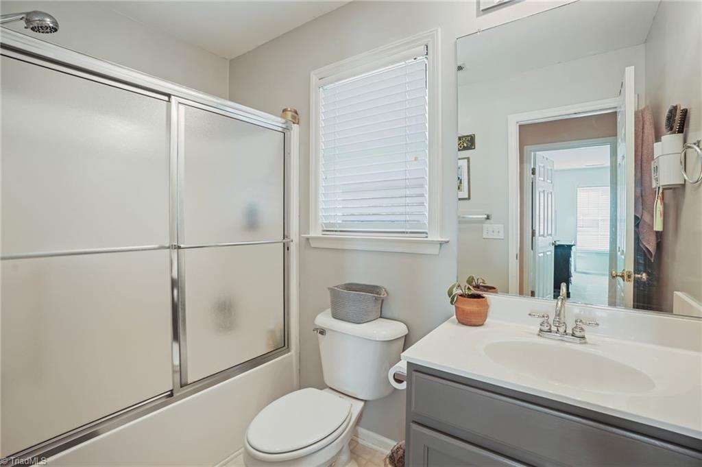 Bathroom with a frosted-glass tub enclosure, gray vanity, and window with white blinds.