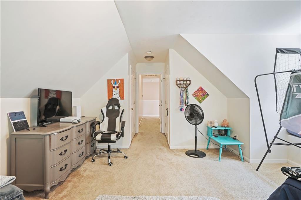 Finished bonus room with sloped ceilings, carpet, and a desk, TV, and gaming chair.