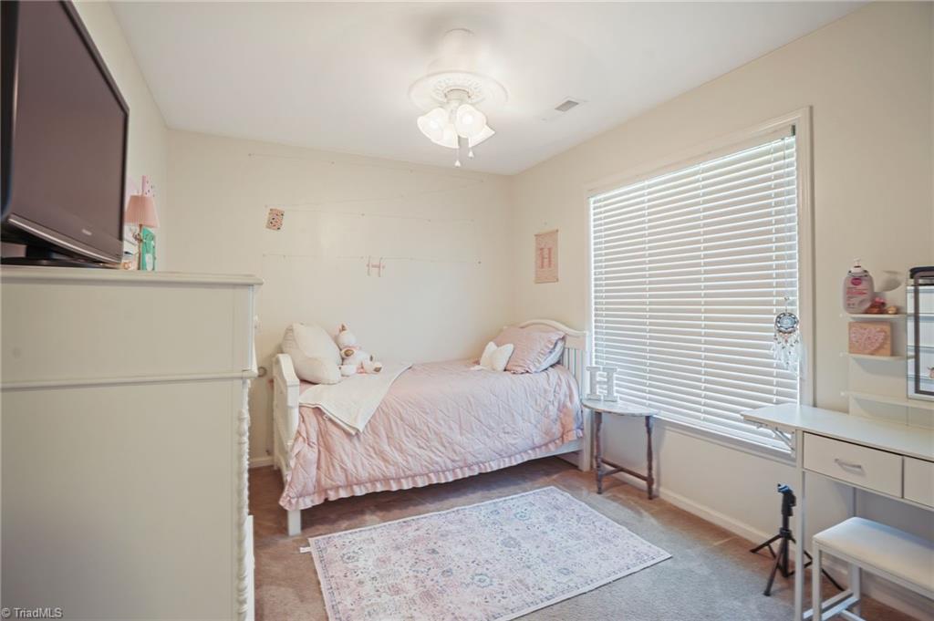 Bedroom with a pink-covered single bed, large window with blinds, and patterned area rug.