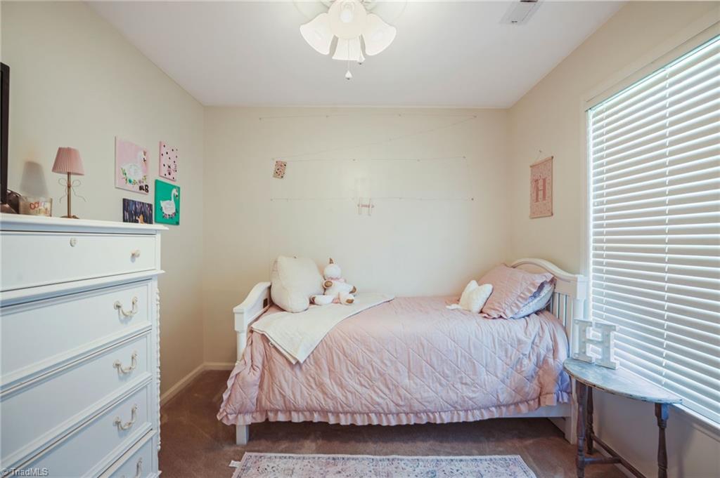 Furnished bedroom with a pink quilted bed beside a large window with white blinds.
