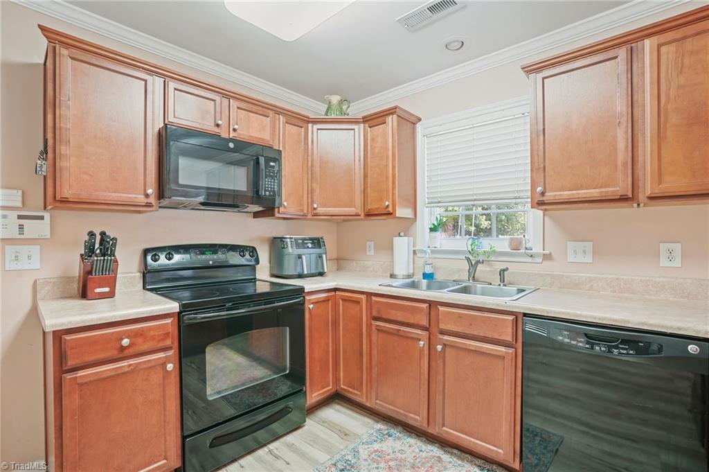 Kitchen with warm wood cabinets, black appliances, and a double-basin sink beneath a window.