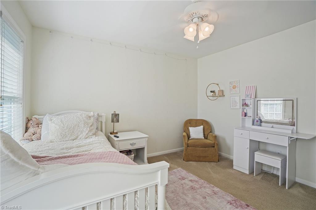 Bedroom with a white bed, blush bedding, tan armchair, and white vanity.