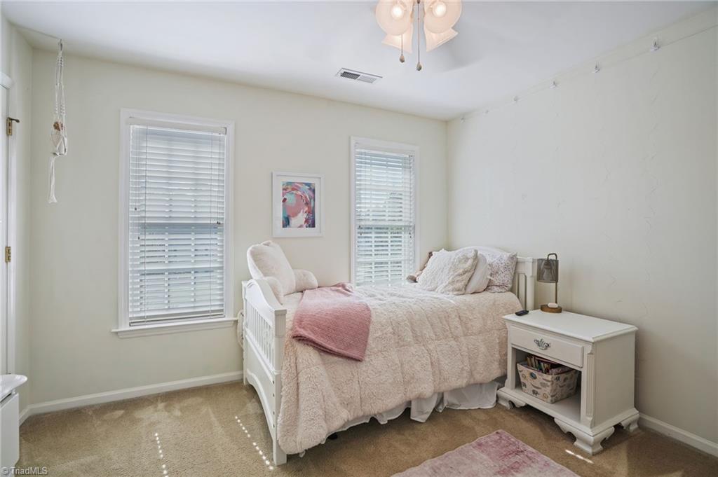 Furnished bedroom with a white daybed, cream bedding, pink throw, and two windows with blinds.
