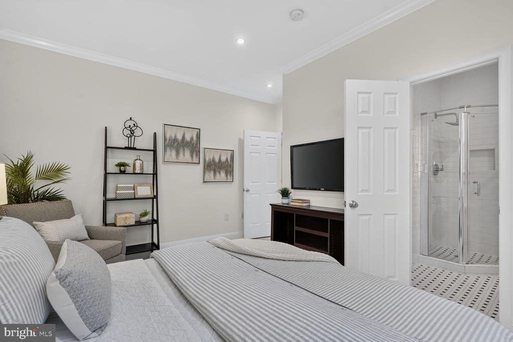 Bedroom with a striped bedspread and sitting area, opening to an ensuite bathroom with a glass shower.