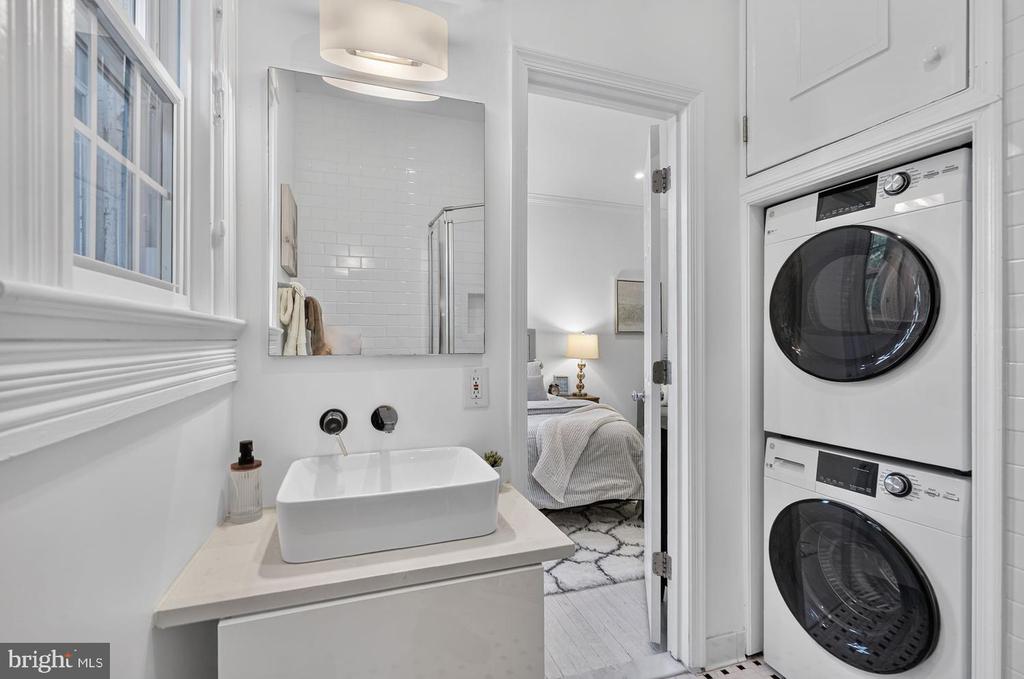 Bathroom with a vessel sink and stacked washer and dryer beside an open bedroom doorway.