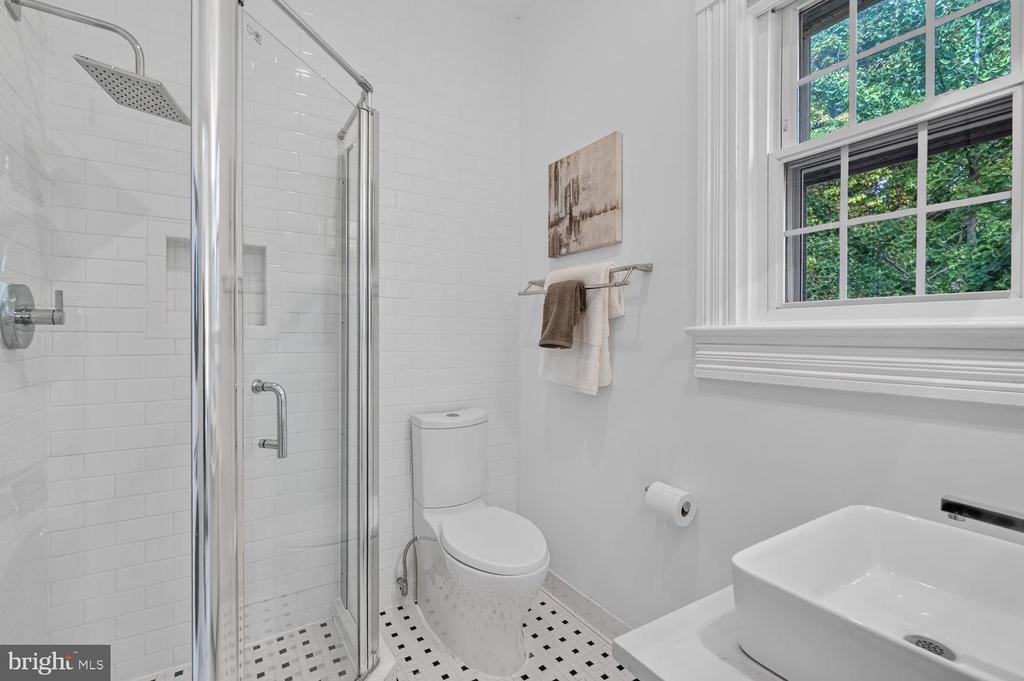 White bathroom with glass shower, mosaic tile floor, vessel sink, and a large window overlooking greenery.