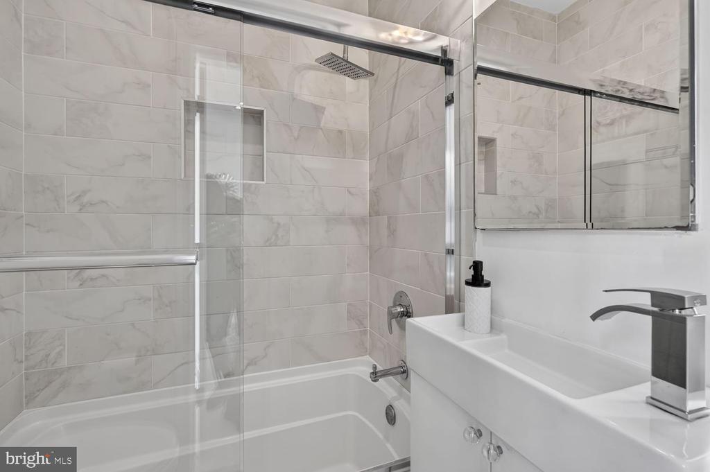 Bathroom with a glass-enclosed tub, marble-look tile, and white vanity.