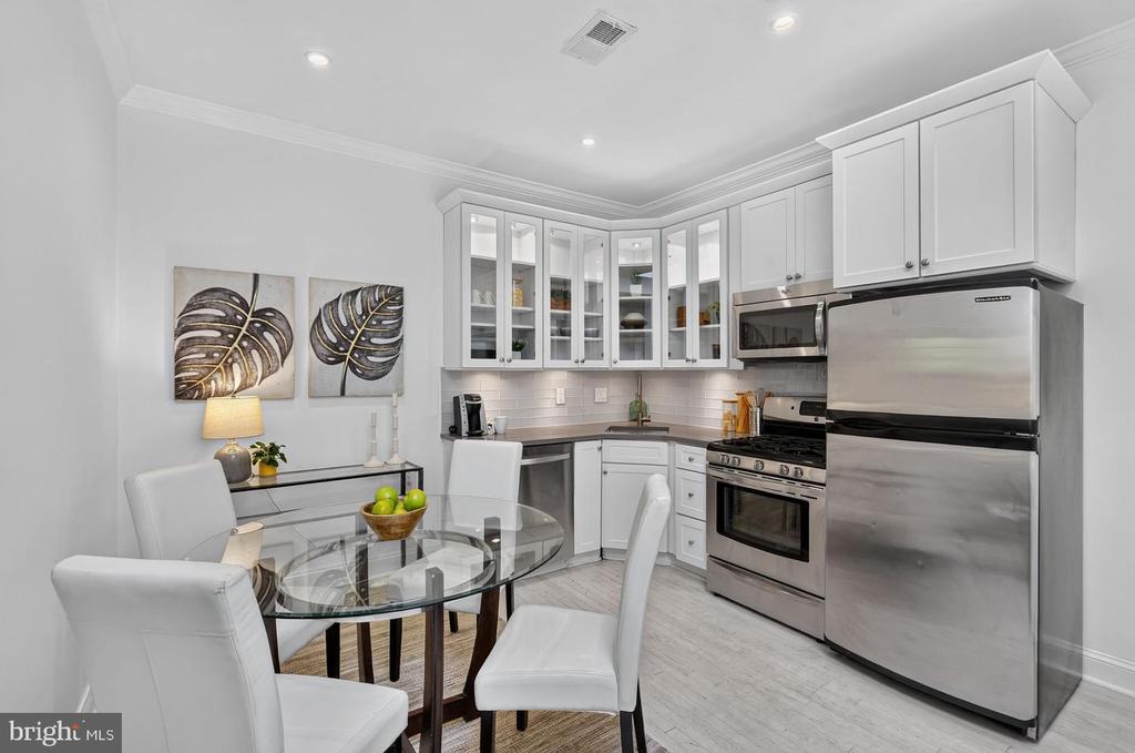 Kitchen and dining area with white cabinets, stainless steel appliances, and a round glass table.