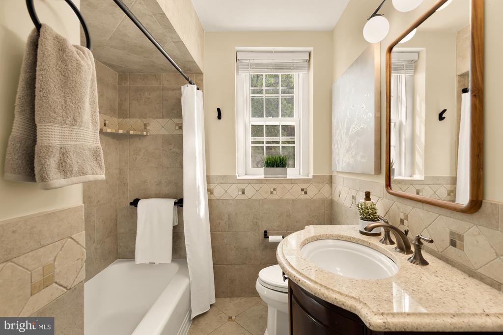 Bathroom with a tiled tub and shower, granite vanity, oval sink, and wood-framed mirror.