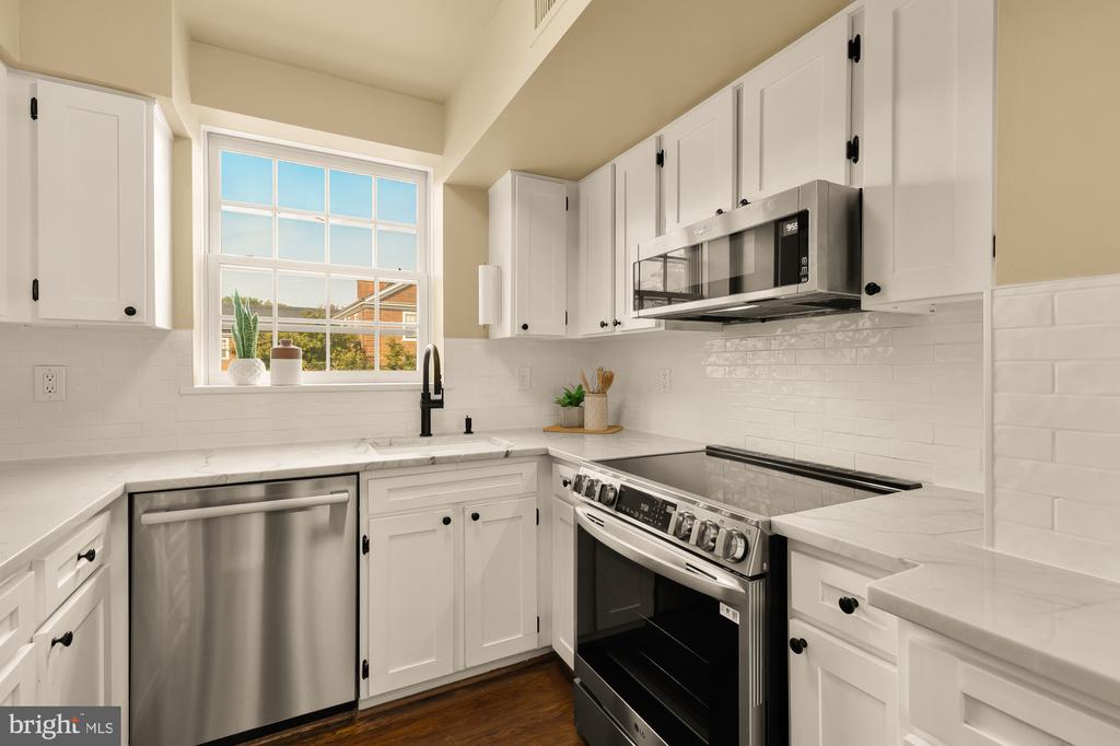 Kitchen with white cabinets, stainless steel appliances, and a large window above the sink.