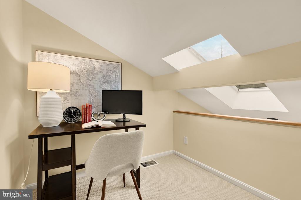 Loft office with a desk and computer beneath two skylights and a sloped ceiling.