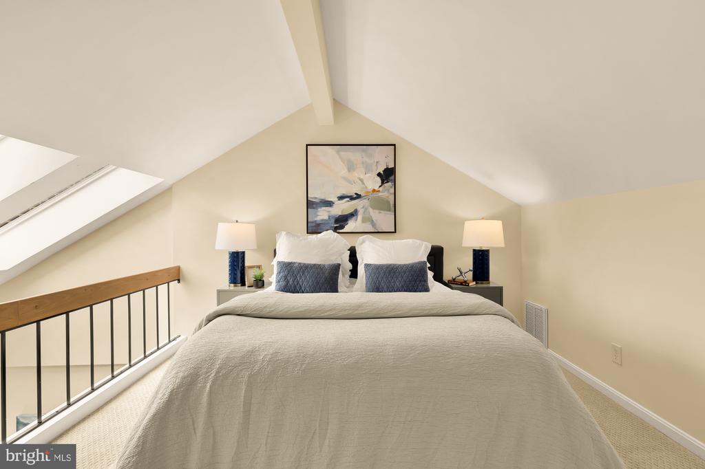 Bedroom with a vaulted ceiling, skylight, and bed beneath framed abstract artwork.